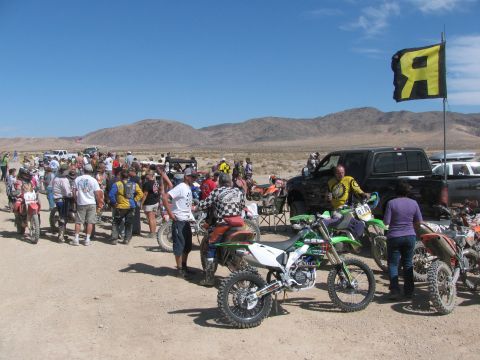 1996 Ford C-350 (Centurion Conversions) - A group of people and dirt bikes are assembled in a dry, dusty area under a clear blue sky.