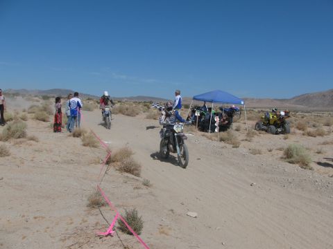 1996 Ford C-350 (Centurion Conversions) - Motorcyclists compete in a desert race, with spectators and support vehicles gathered under a canopy.