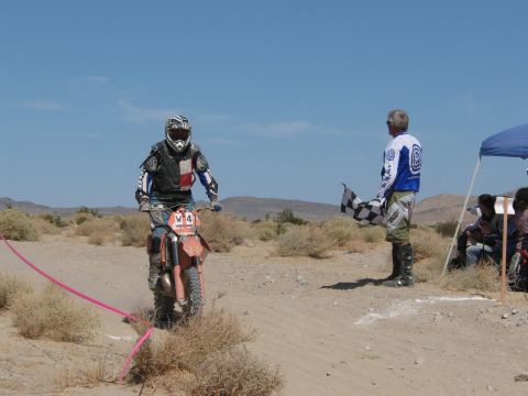 1996 Ford C-350 (Centurion Conversions) - A dirt bike racer is about to cross the finish line as a person waves a checkered flag.