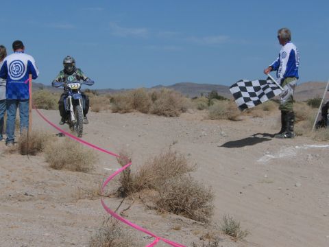 1996 Ford C-350 (Centurion Conversions) - A dirt bike rider is about to cross the finish line as a man waves a checkered flag.