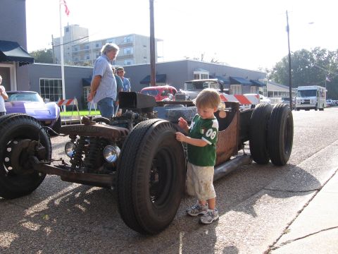 1967 Ford Mustang - A child inspects a custom hot rod with a prominent engine and large tires on a street.