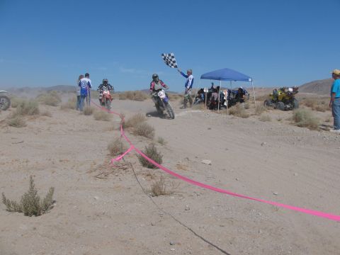 1996 Ford C-350 (Centurion Conversions) - A motorcyclist crosses the finish line at a desert race as a checkered flag is waved.