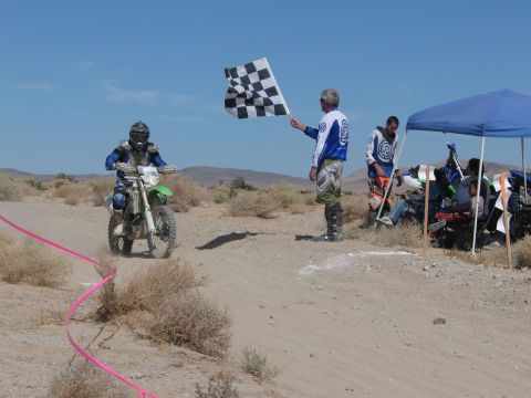 1996 Ford C-350 (Centurion Conversions) - A dirt bike rider is about to cross the finish line as an official waves a checkered flag at a desert race.