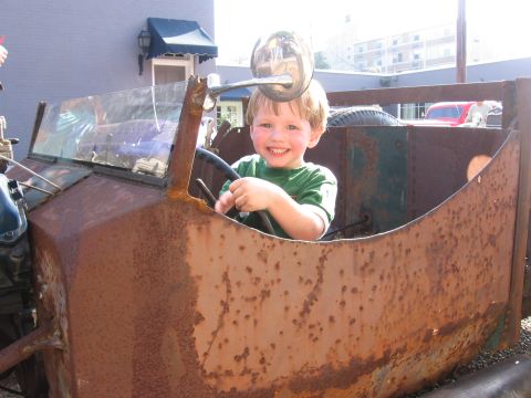 1967 Ford Mustang - A young boy happily sits behind the steering wheel of a very old, corroded vehicle.