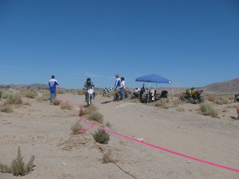 1996 Ford C-350 (Centurion Conversions) - A desert race scene with a dirt bike rider, spectators, and ATVs under a clear blue sky.