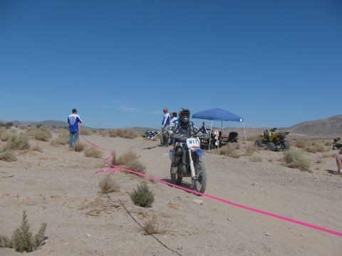 1996 Ford C-350 (Centurion Conversions) - A desert race scene with a dirt bike rider navigating a course marked by a pink ribbon, with an ATV visible in the distance.