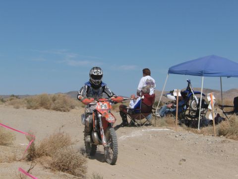 1996 Ford C-350 (Centurion Conversions) - A dirt bike rider with the number F8 on their front plate navigates a desert course, with spectators and another motorcycle visible.