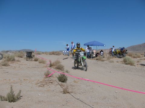1996 Ford C-350 (Centurion Conversions) - A dirt bike racer navigates a sandy course during an event, with spectators and other vehicles in the background.