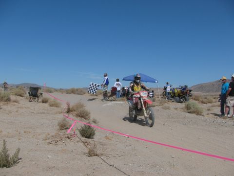 1996 Ford C-350 (Centurion Conversions) - A dirt bike rider crosses the finish line at a desert race, with spectators and other vehicles present.