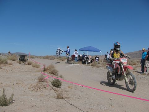 1996 Ford C-350 (Centurion Conversions) - Motorcycle race finishes in a desert setting with a checkered flag and spectators under a blue sky.