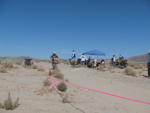 1996 Ford C-350 (Centurion Conversions) - A dirt bike race is underway with participants, support crews, and ATVs gathered under tents in a desert environment.