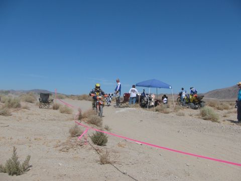 1996 Ford C-350 (Centurion Conversions) - Participants in a desert dirt bike race near a finish line with tents and an ATV.
