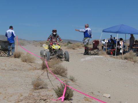 1996 Ford C-350 (Centurion Conversions) - A quad bike racer navigates a desert course while an official directs them.