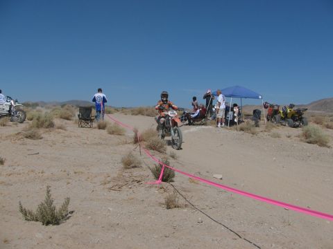 1996 Ford C-350 (Centurion Conversions) - A dirt bike rider navigates a sandy course while spectators watch from the shade of a canopy.
