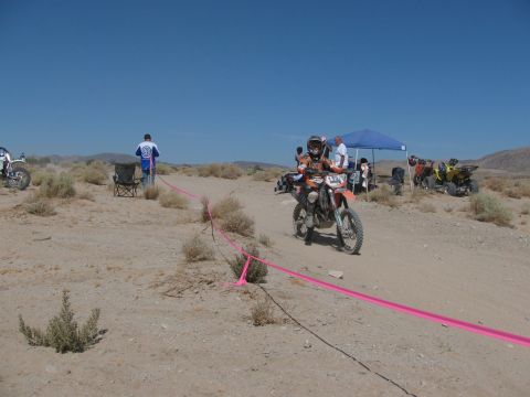 1996 Ford C-350 (Centurion Conversions) - A dirt bike rider navigates a course marked by pink tape in a desert environment, with spectators and other vehicles present.