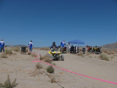 1996 Ford C-350 (Centurion Conversions) - A desert race event with participants and spectators gathered under a canopy, with quad bikes visible on the track.