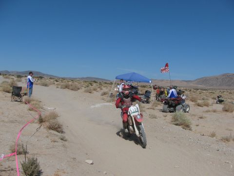 1996 Ford C-350 (Centurion Conversions) - A dirt bike racer navigates a sandy course during an event, with spectators and other vehicles present.
