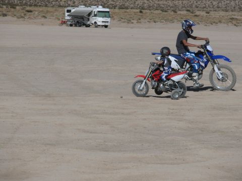 1996 Ford C-350 (Centurion Conversions) - Two dirt bikes are ridden by children in a desert area, with an RV parked in the background.
