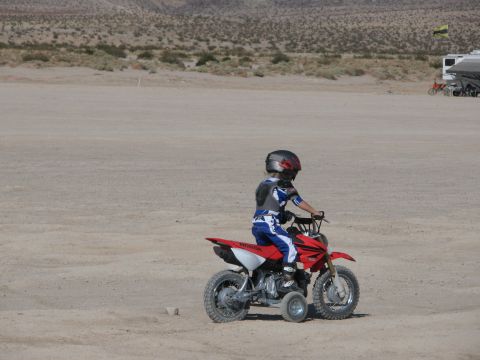 1996 Ford C-350 (Centurion Conversions) - A child in racing gear rides a red dirt bike equipped with training wheels in a desert landscape.