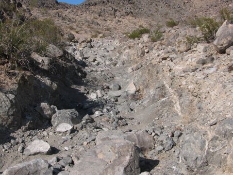 1996 Ford C-350 (Centurion Conversions) - A dry creek bed winds through a rocky desert landscape under a clear blue sky.