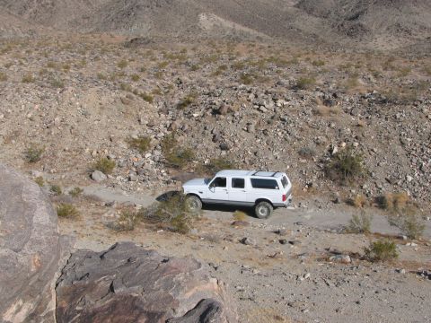 1996 Ford C-350 (Centurion Conversions) - White 1996 Ford C-350 (Centurion Conversions) SUV driving on a dirt road in a rocky, arid environment.