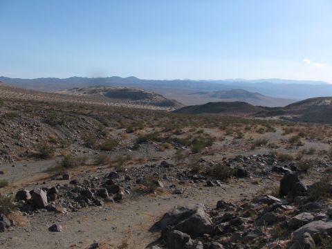 1996 Ford C-350 (Centurion Conversions) - A wide view of a dry, rocky desert landscape with rolling hills in the distance under a clear blue sky.