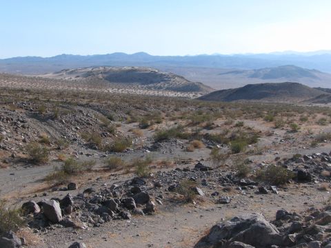 1996 Ford C-350 (Centurion Conversions) - A wide view of a dry, rocky desert terrain with sparse vegetation and distant hills under a bright sky.