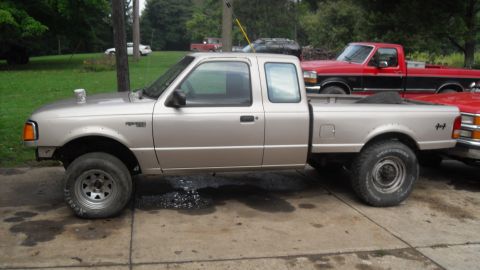 1997 Ford Ranger - Side view of a tan Ford Ranger 4x4 extended-cab pickup on a paved driveway, with a red Ford pickup parked behind it.