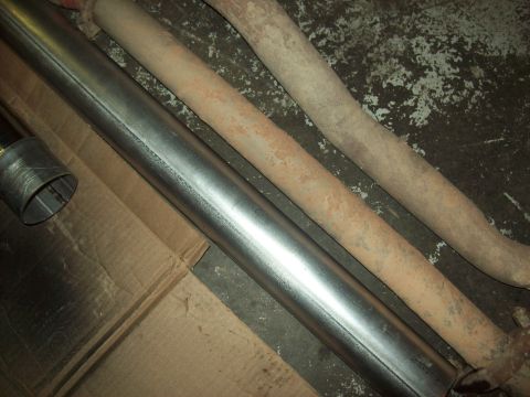 1985 Ford Bronco - A new exhaust pipe lies next to two older, rusted pipes on a cardboard surface.