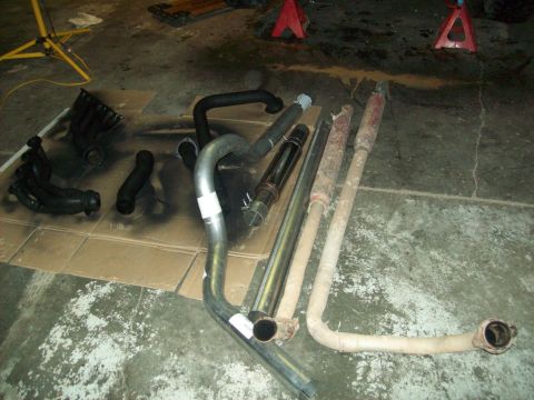 1985 Ford Bronco - Collection of exhaust system components, including headers and mufflers, are arranged on the floor.