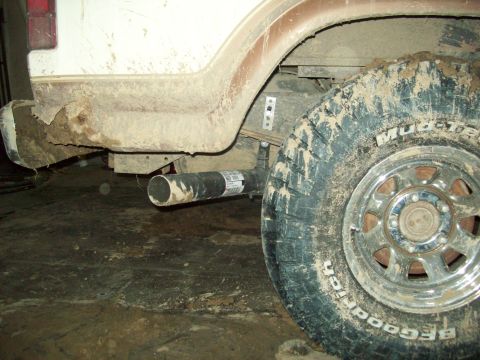 1985 Ford Bronco - The rear tire and exhaust pipe of a dirty vehicle are visible from the side.
