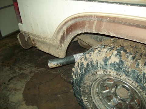 1985 Ford Bronco - Close-up view of a vehicle's exhaust pipe and heavily muddied tire, showing part of the rear bodywork.