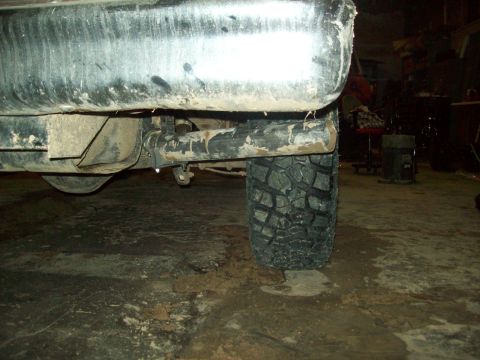 1985 Ford Bronco - Close-up of a truck's rear tire and bumper, with visible mud and dirt on the undercarriage.