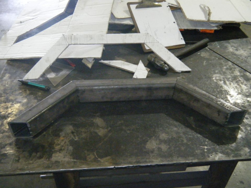 Metal tubing bent into shape on a workbench with cardboard templates nearby