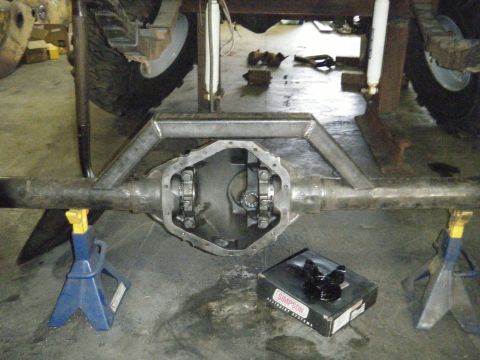 1978 Ford Bronco - Rear axle assembly on jack stands, with the differential cover removed and a box of parts on the floor.