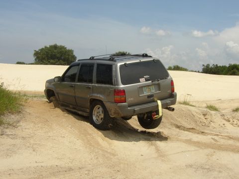 1991 Ford Bronco - A Jeep Grand Cherokee is stuck in a sand dune with its rear passenger side wheel lifted.