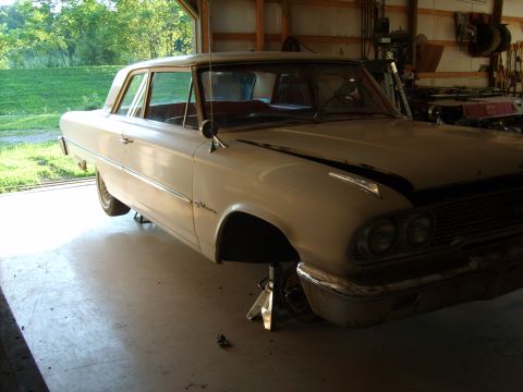 1963 Ford Galaxie - A white 1963 Ford Galaxie sedan is parked on jack stands inside a garage, with the front end visible.