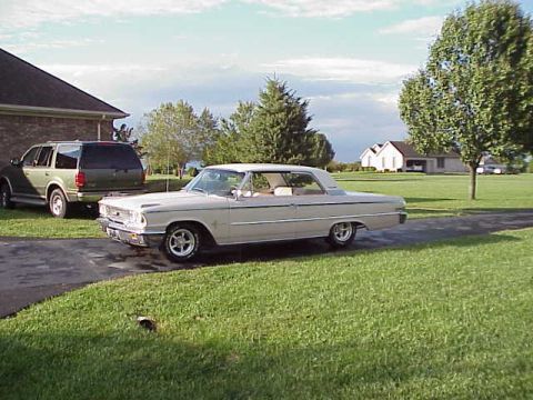 1963 Ford Galaxie - A tan 1963 Ford Galaxie is parked on a driveway next to a green SUV, with houses and trees in the background.