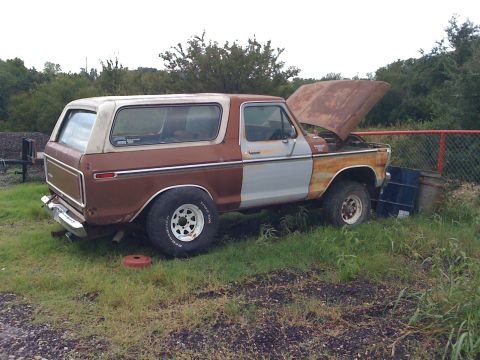 1978 Ford Bronco - A rusty 1978 Ford Bronco sits in a field with its hood up, showing signs of wear and tear.