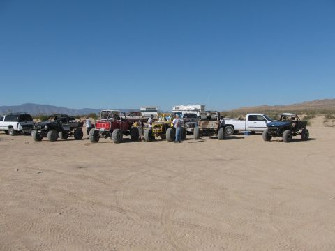 1996 Ford C-350 (Centurion Conversions) - Group of off-road vehicles and trucks gathered in a desert setting.