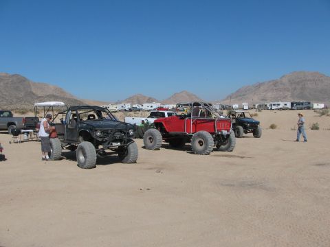 1996 Ford C-350 (Centurion Conversions) - Modified off-road vehicles and RVs are parked in a desert area with mountains in the background.