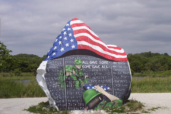 War memorial stone with American flag and painted soldiers, listing names
