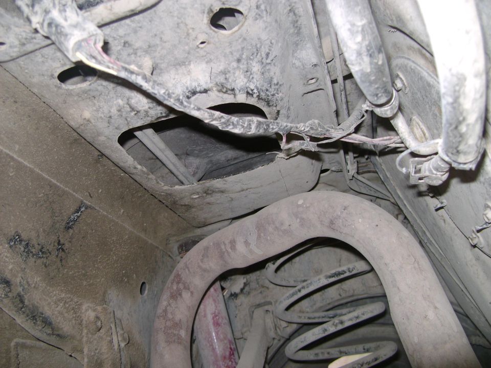 underbody view showing exhaust pipe, suspension spring, and wiring harness