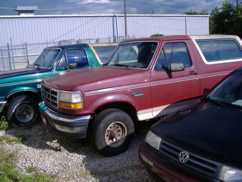 1992 Ford Bronco - Two Ford Broncos, one red and one green, are parked outdoors next to a building.