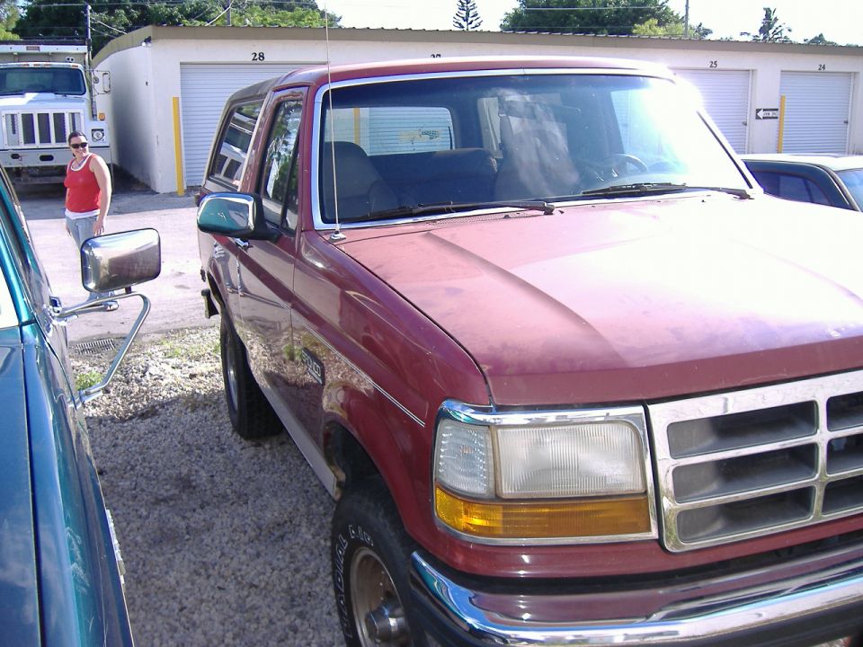 Red 1992 Ford Bronco parked on gravel by white storage units, seen from front passenger side.