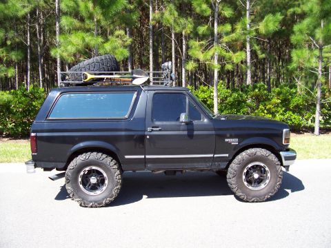 1994 Ford Bronco - This black Ford Bronco is equipped with a roof rack, spare tire, and shovel, ready for adventure.