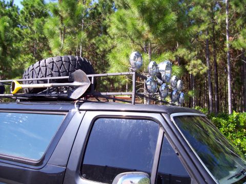 1994 Ford Bronco - 1994 Ford Bronco with a roof rack loaded with a spare tire and shovel, plus several spotlights.