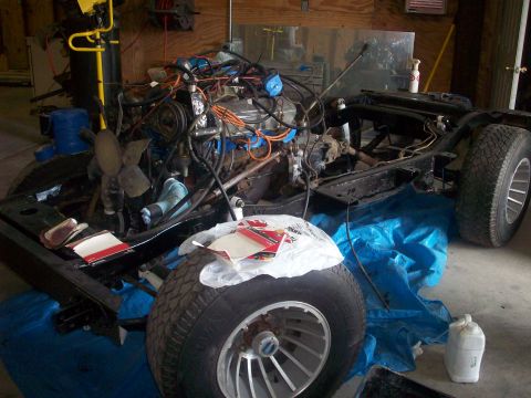 1978 Jeep CJ5 - A vehicle's chassis and engine are disassembled and laid out on a blue tarp in a workshop.