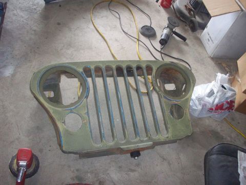 1978 Jeep CJ5 - A Jeep grille, likely undergoing restoration, rests on a workshop floor surrounded by tools and supplies.