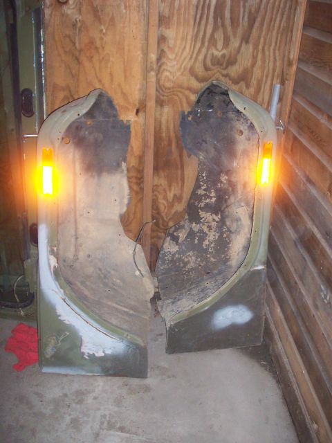 1978 Jeep CJ5 - Two heavily damaged Jeep CJ5 doors are leaning against a wooden wall, with one door's turn signal light on.